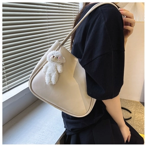 Détail d'un sac hobo crème avec breloque ours en peluche porté par un mannequin