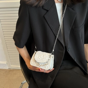 White jacquard chain crossbody bag with floral texture and silver strap on black suit