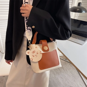 Chic color-block crossbody bag with wide printed strap and cute tiger charm in office setting