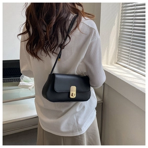 Minimalist black leather underarm bag with gold clasp shown on model shoulder