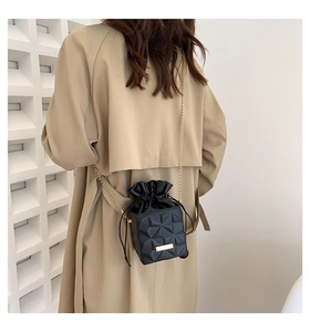 Detail of black quilted crossbody bag with gold chain and velvet drawstring closure