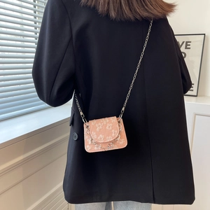 Pink mini crossbody bag with floral texture and heart pendant chain on black blazer