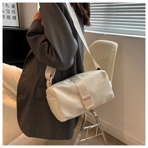 Detail view of a cream-colored waterproof cylinder crossbody bag with wide strap on model
