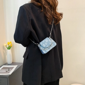 Blue floral mini crossbody bag with silver chain strap worn by a model in casual style