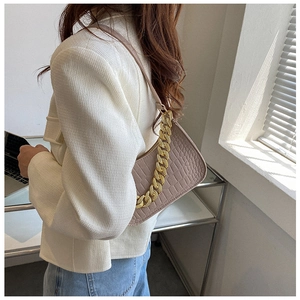 Detail of light brown crocodile embossed underarm bag with decorative gold chain strap
