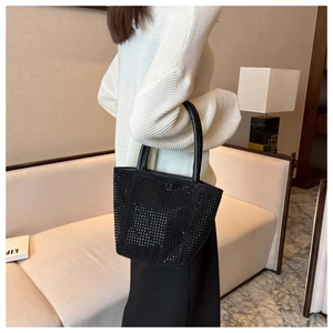 Close-up of a black rhinestone bucket bag with dual handles shown in a modern interior