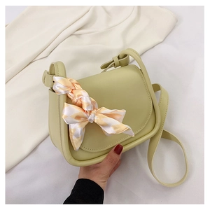 Dettaglio borsa a sella verde chiaro con elegante sciarpa di seta su tessuto bianco