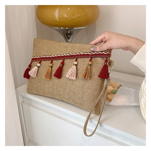 Detail of hand-held woven linen envelope bag with colorful tassels and red stripe trim