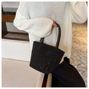 Detail of a chic black rhinestone bucket bag held by a model wearing a white sweater