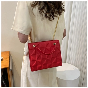 Détail du sac bandoulière rouge matelassé avec chaîne dorée et texture pyramidale