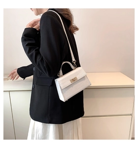 Detail of white crocodile texture bag with gold twist lock on black blazer