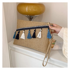 Detail view of woven envelope clutch with bohemian fringe tassels and blue patterned strap