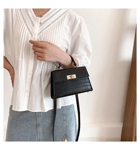 Close-up of black crocodile embossed leather handbag with golden twist lock and top handle