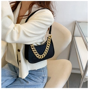 Detail of black crocodile pattern underarm bag with decorative gold chunky chain strap