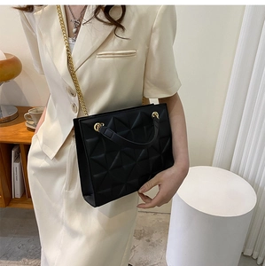 Détail du sac à main noir matelassé géométrique avec chaîne dorée sur un mannequin