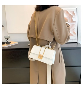 White faux crocodile skin crossbody bag with gold chain strap shown on a model