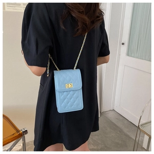 Close-up of sky blue quilted crossbody bag with gold twist lock and chain strap on shoulder