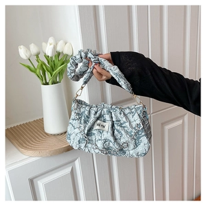 Détail d'un sac plissé bleu clair avec chaîne florale argentée et étiquette de marque NGPIN