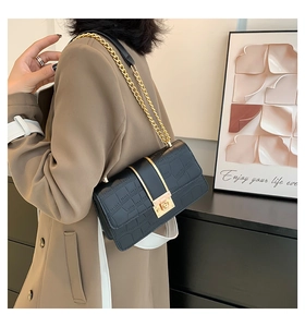 Detail of black crocodile texture bag with gold metal buckle and chain strap on shoulder