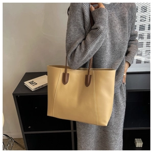 Detail of a large beige tote bag with brown handles on a model in a minimalist setting