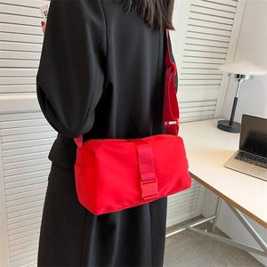 Minimalist red waterproof crossbody bag with wide shoulder strap shown on a black coat