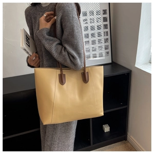 Close-up of mustard yellow leather tote bag with dark brown straps on grey knitwear
