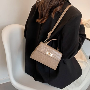 Khaki crocodile pattern crossbody bag with gold buckle shown on shoulder of a model