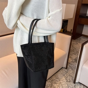 Minimalist black rhinestone bucket bag with a top handle held by a model in a cozy room