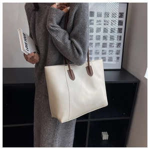 Detail of a creamy white tote bag featuring vertical stitching and brown shoulder straps