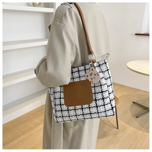 Close-up of checkered tote bag with brown leather pocket and white cat pendant charm