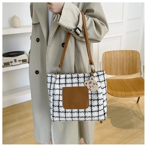 Detail of checkered tote bag with brown leather pocket and cute cat keychain charm