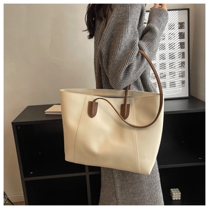 Detail view of cream tote bag with brown straps worn by a model in a minimal room