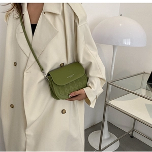 Green saddle bag detail with quilted texture and fashion logo on beige trench coat