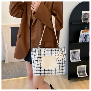 Detail of checkered tote bag featuring a cute cat charm and cream leather handles