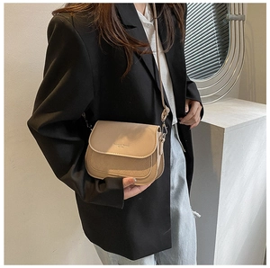 Detail of beige quilted saddle bag with adjustable strap worn by model for daily commute