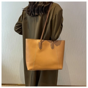 Minimalist light brown tote bag shown from back view on olive green coat