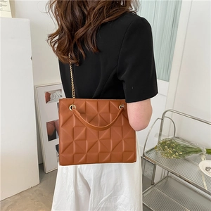 Sac bandoulière marron matelassé avec chaîne porté par un mannequin en intérieur