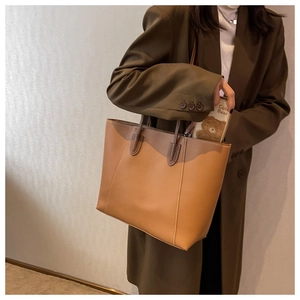 Brown leather tote bag featuring contrast stitching shown being worn with a blazer