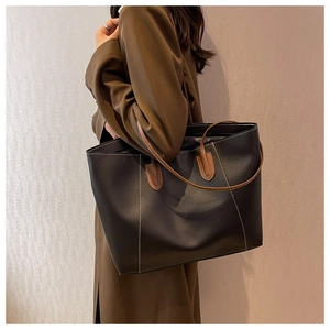 Detail of minimalist black tote bag featuring white contrast stitching and brown leather strap