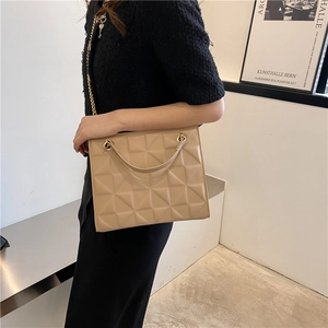 Sac bandoulière matelassé beige avec chaîne dorée porté par un mannequin en décor moderne