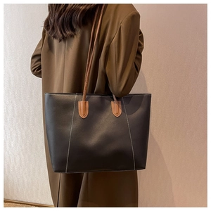 Detail of a large black tote bag with brown straps and white stitching on a wool coat