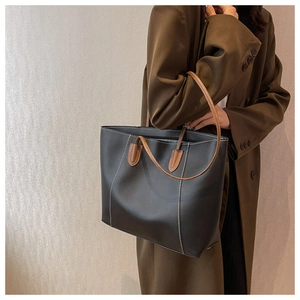 Detail of contrast white stitching and brown leather handles on a black tote bag