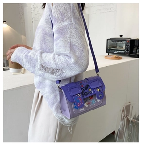 Détail d'un sac messager graffiti violet porté par un mannequin dans une pièce blanche