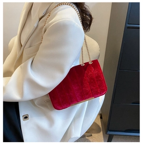 Détail d'un sac à bandoulière en velours rouge avec matelassage et chaîne en métal doré