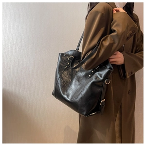 Detail of black tote bag with retro oily leather texture on a female model in brown suit