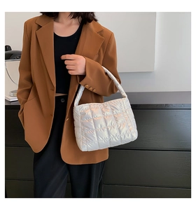 Close-up of white quilted handbag with metallic finish worn with a brown blazer