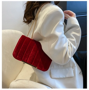 Détail du sac bandoulière en velours rouge avec chaîne dorée sur blazer blanc