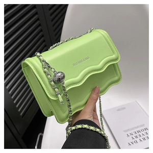 Detail of neon green flap crossbody bag with wavy edges and silver chain strap