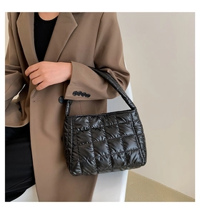 Detail view of a black quilted puffer tote bag on shoulder with shiny nylon finish