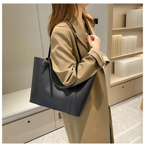 Side view of a large black faux leather tote bag worn by a model in a modern office
